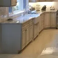 Glazed cream cabinets around a white farmhouse sink with a grey stone countertop and polished floor