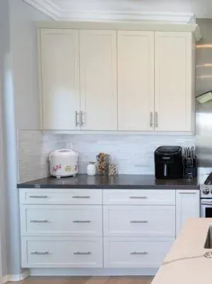 White shaker kitchen cabinets with brushed pulls above a dark countertop and a white tile backsplash