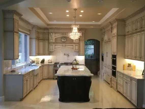 Cream cabinet kitchen with a tray ceiling, crystal chandelier and a dark wood island topped with white marble