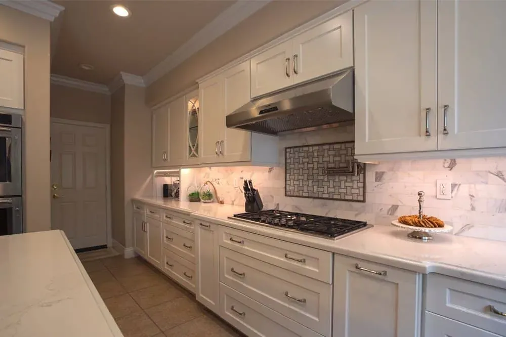 Kitchen with white raised-panel cabinetry, a stainless range hood and a patterned tile backsplash over the cooktop