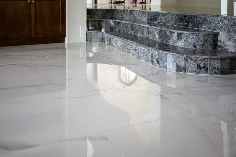 Glossy white marble-look floor tile beside a curved raised platform edged in dark gray stone tile