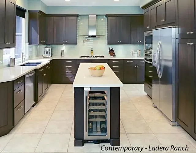 Dark cabinet kitchen island with a built-in wine cooler beside a stainless refrigerator