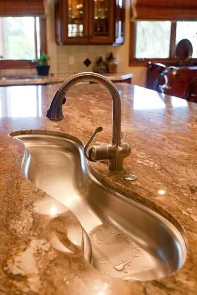 Curved stainless sink and gooseneck faucet on a swirled reddish-brown granite countertop with cabinets behind