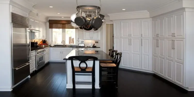 White kitchen with a black island, overhead hanging pot rack and dark hardwood flooring