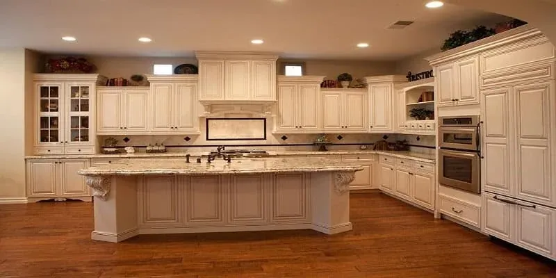 Cream ornate cabinets with a large granite-topped island, corbels, wood flooring and a built-in refrigerator column