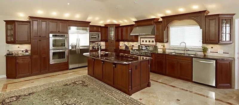 cherry wood kitchen with black granite island, stainless double ovens and patterned area rug