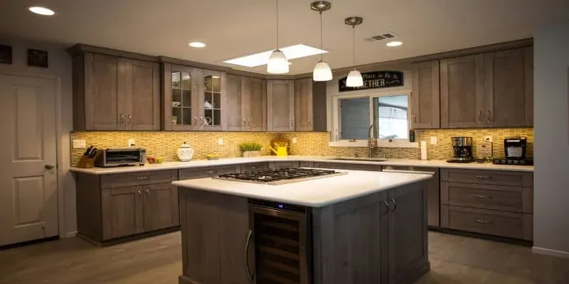 Grey wood kitchen with an island cooktop, white countertops, a skylight and three pendant lights