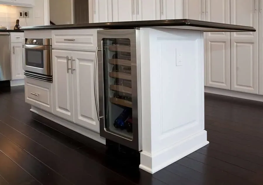 White raised-panel island with a built-in wine fridge and microwave drawer on a dark wood floor