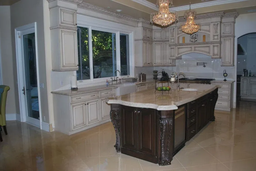 Kitchen with two chandeliers above a dark carved island and a window wall