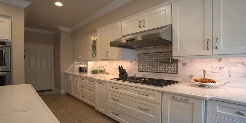 White cabinet run with a stainless range hood, gas cooktop and a mosaic tile backsplash accent