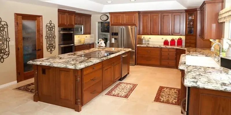Medium wood kitchen with a granite island cooktop, stainless refrigerator and decorative area rugs