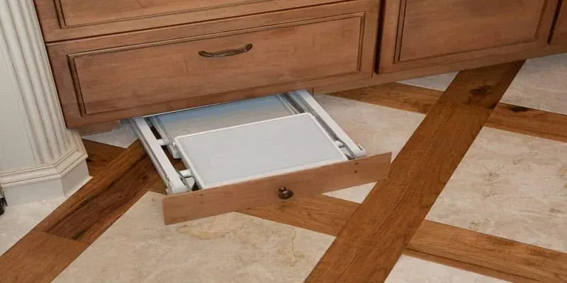 wood cabinet with a pulled-out drawer tray beside a herringbone wood-look tile floor pattern