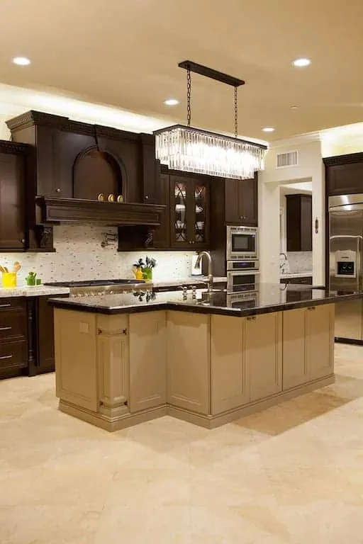 Dark cabinet kitchen with a cream island base topped by a large crystal chandelier