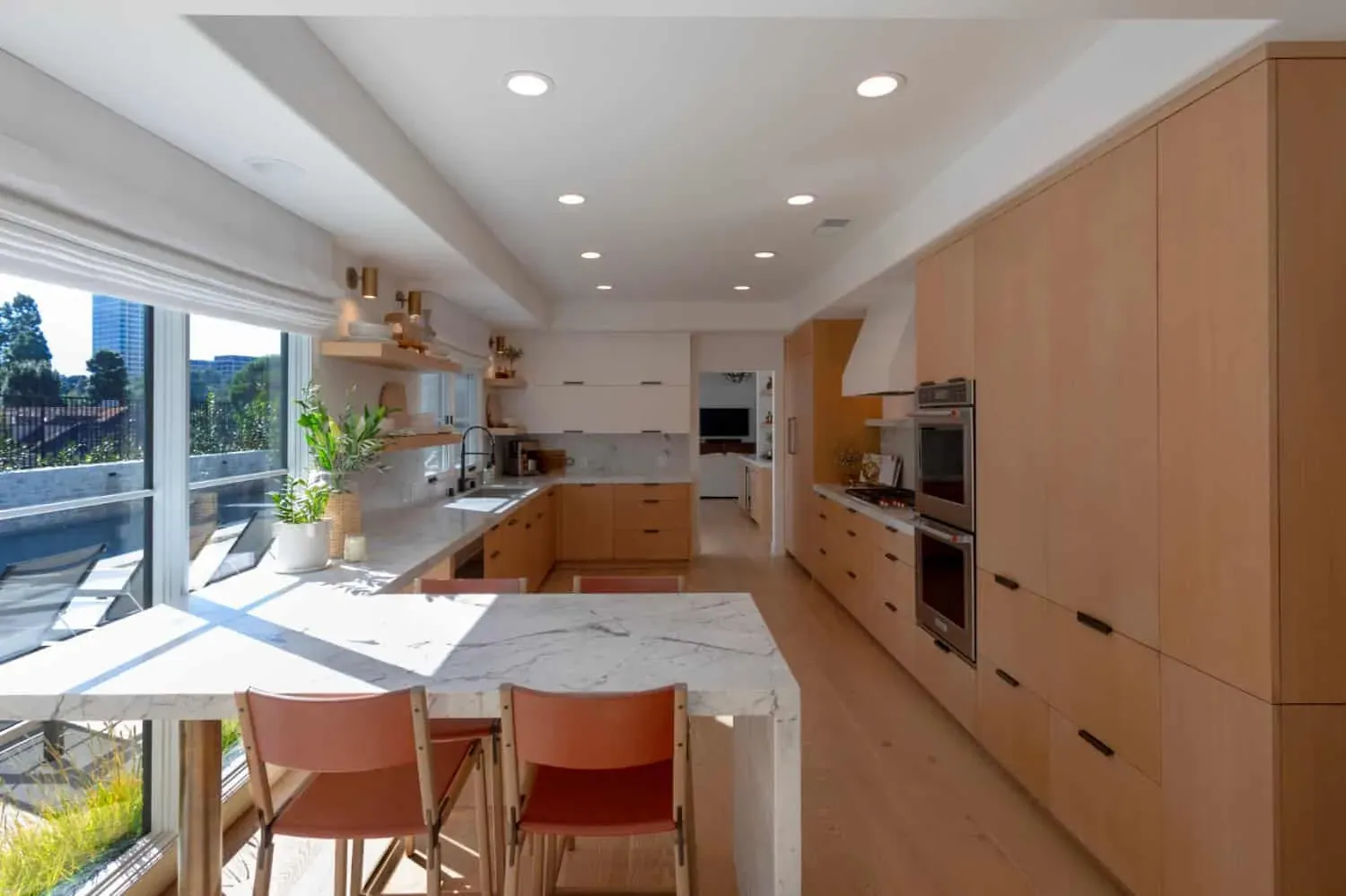 Light oak slab-front kitchen with a marble waterfall island and terracotta bar stools