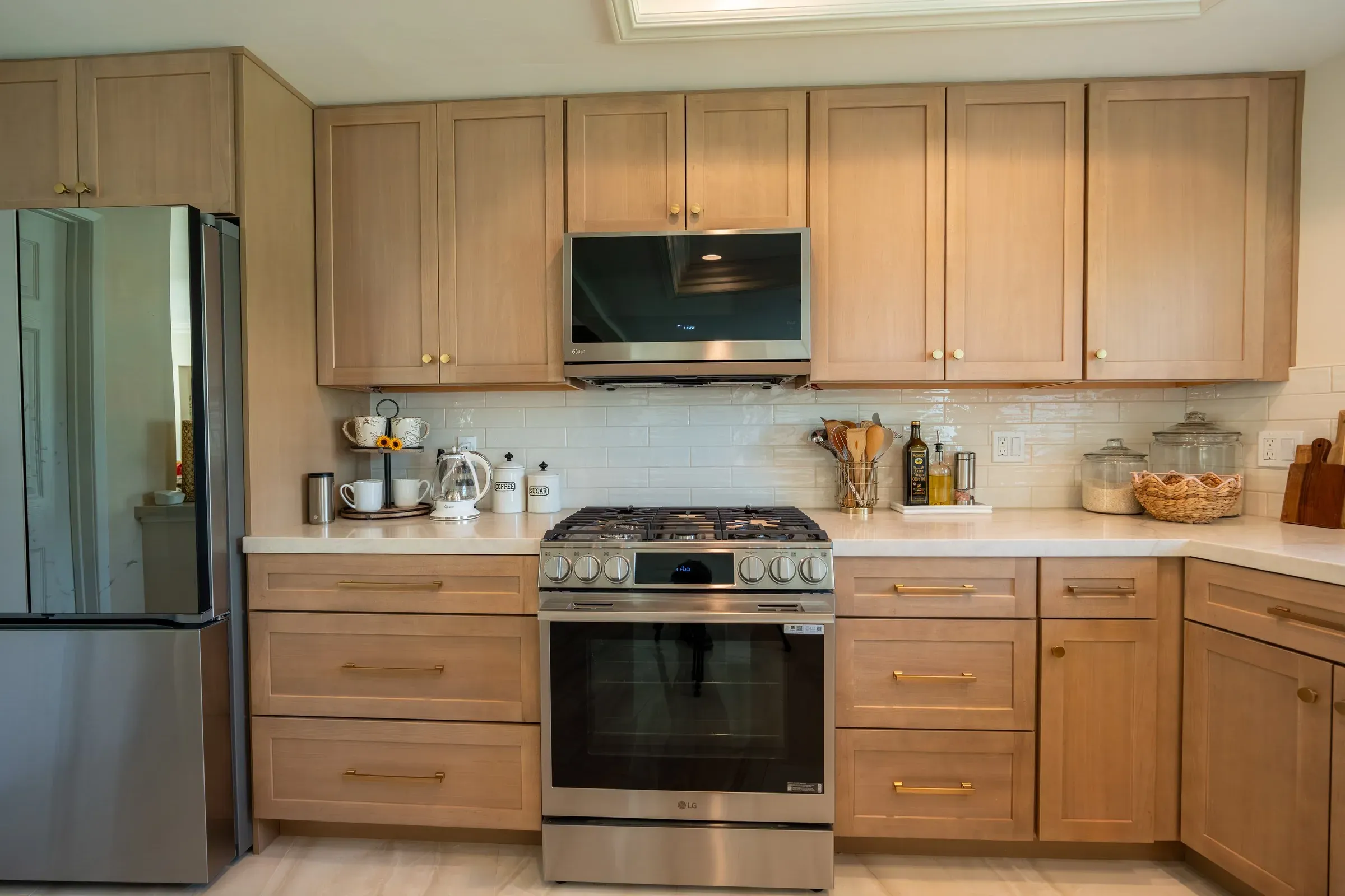 Light oak shaker cabinets around a stainless gas range and microwave below white subway tile