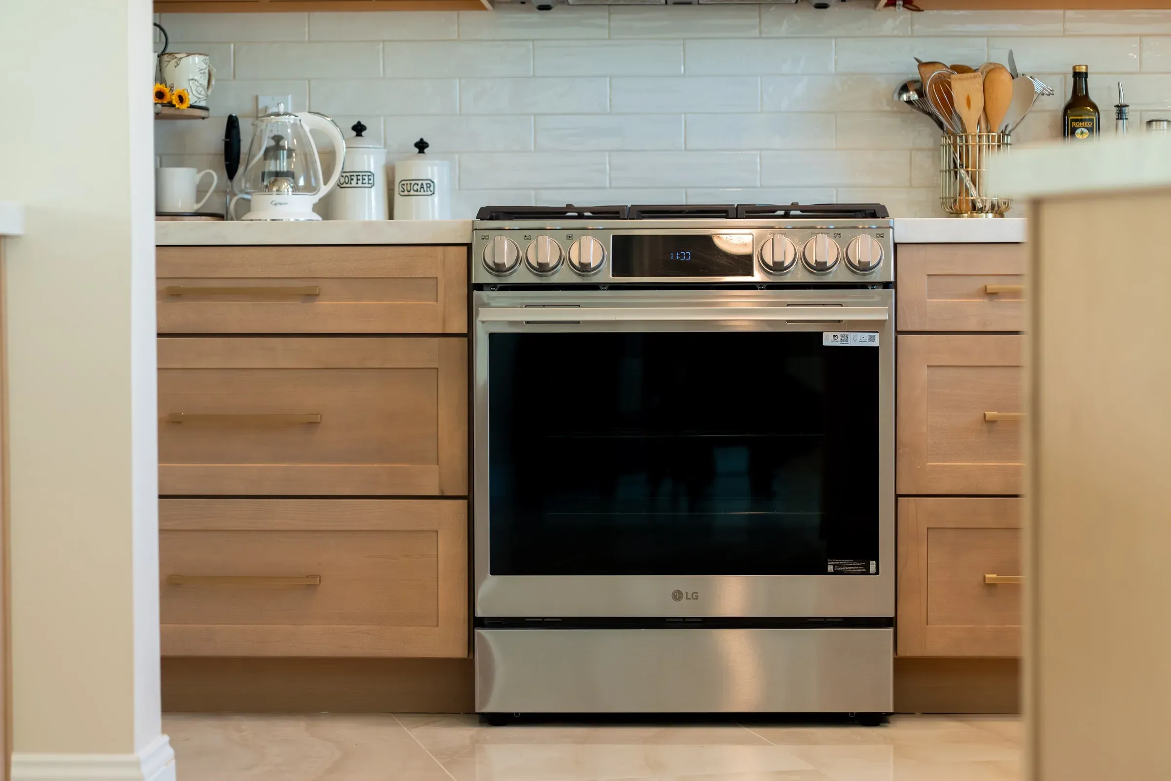 Light oak shaker drawer stacks with brass pulls on both sides of a stainless range below a white tile backsplash