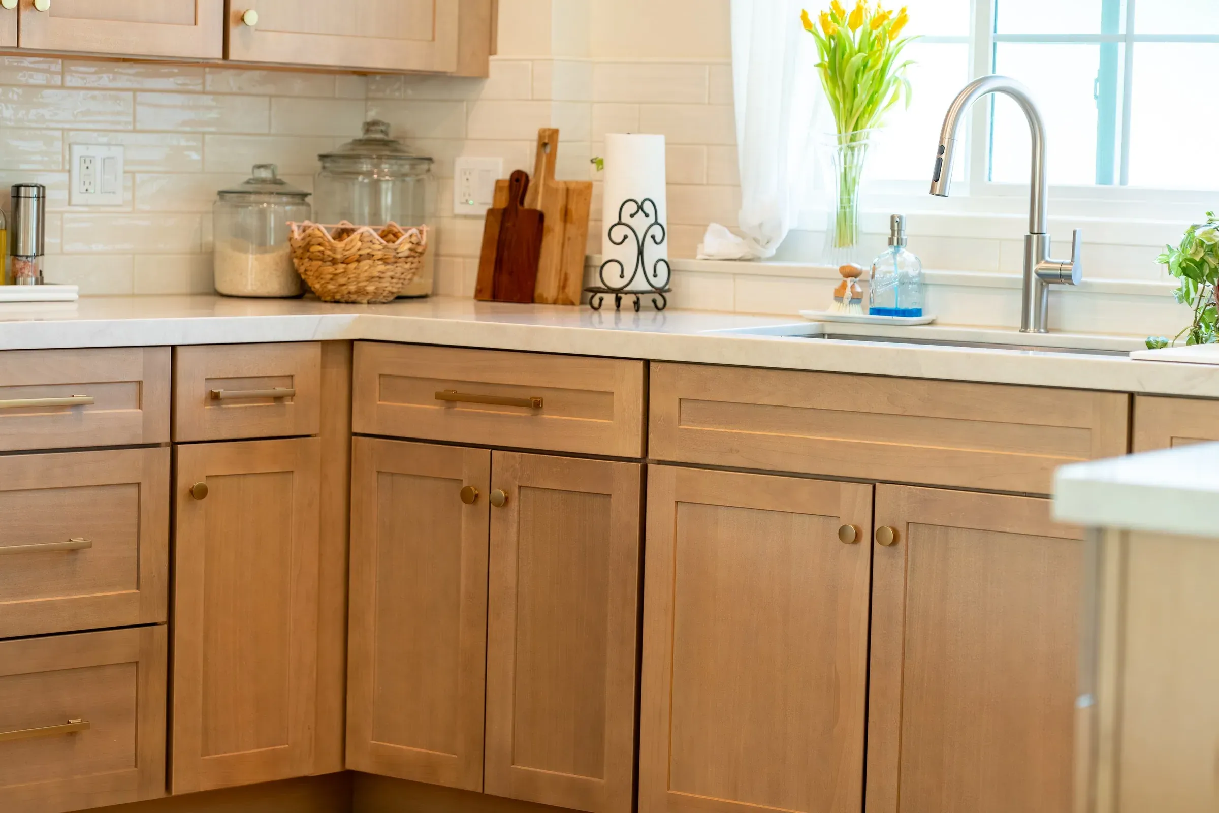 Light oak shaker base cabinets with brass pulls under a pale counter, glossy subway tile and a window over the sink