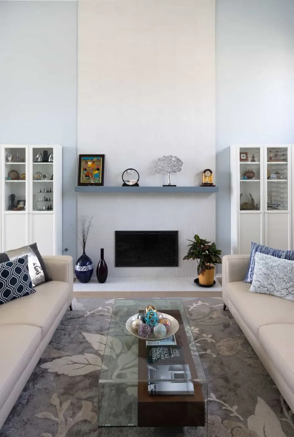White built-in cabinets with glass-front uppers flanking a fireplace below a floating shelf