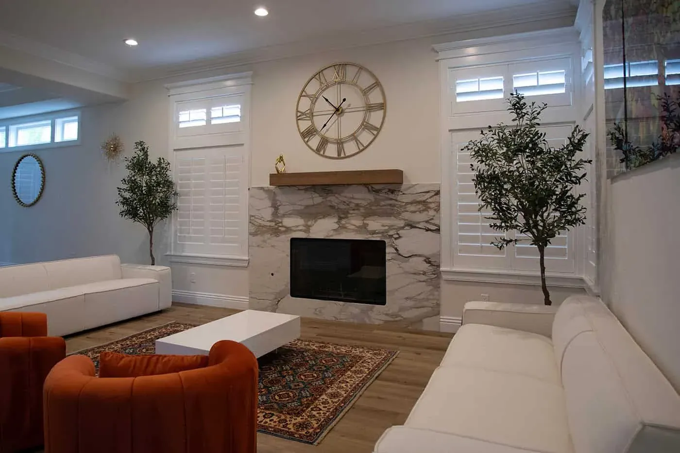 Living room with a white veined slab fireplace wall, a large wall clock, white sofas and two orange armchairs