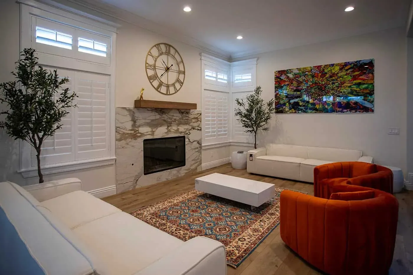 Living room with a white veined slab fireplace surround, wide-plank wood flooring, white sofas and orange armchairs