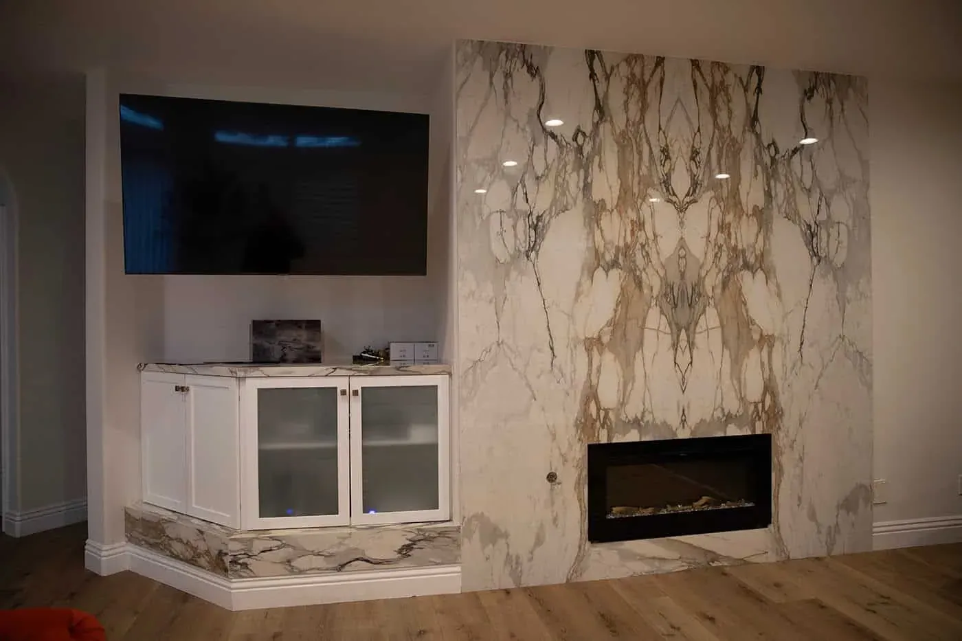 Floor-to-ceiling white slab with bold gold and grey veining around a linear fireplace below a wall-mounted television