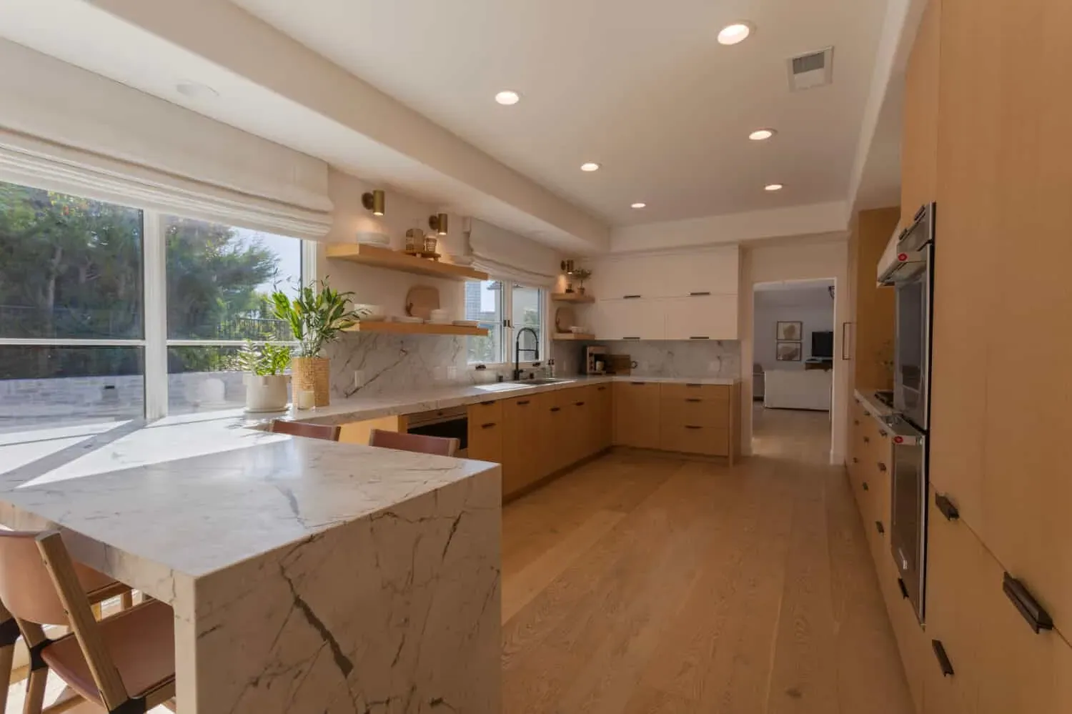 Light wood plank flooring running the length of an oak kitchen past a marble waterfall island