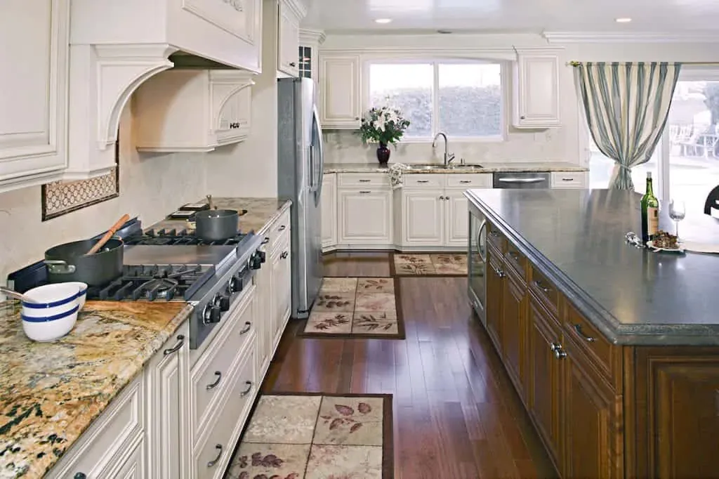Long cream kitchen with a grey-topped island, a range under a plaster hood and windows