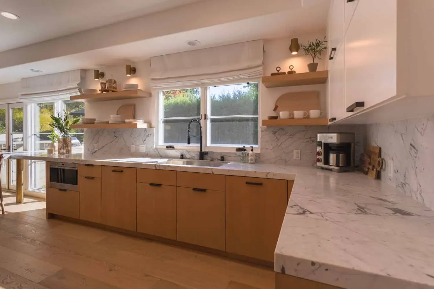 Oak kitchen cabinetry with a marble backsplash and a sink beneath a wide window over the garden