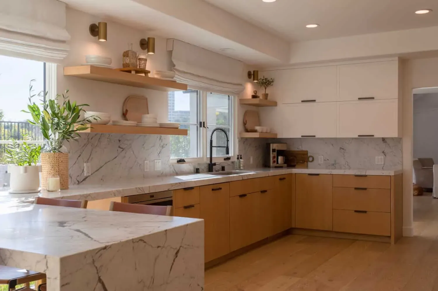 Oak cabinetry under open shelving with marble counters and a black tap