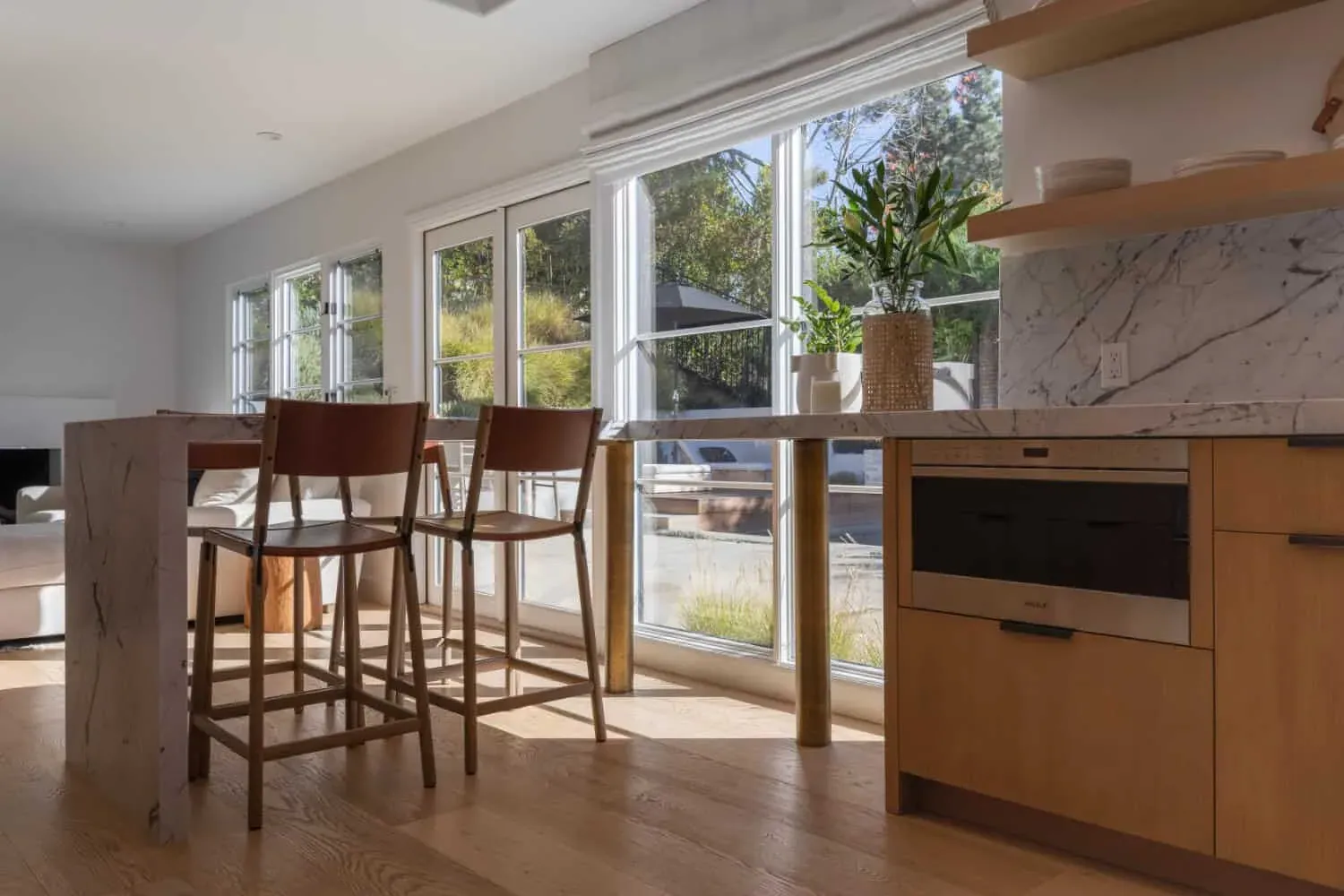 Oak kitchen with bar stools at an island and a wood floor running to sliding doors onto the garden
