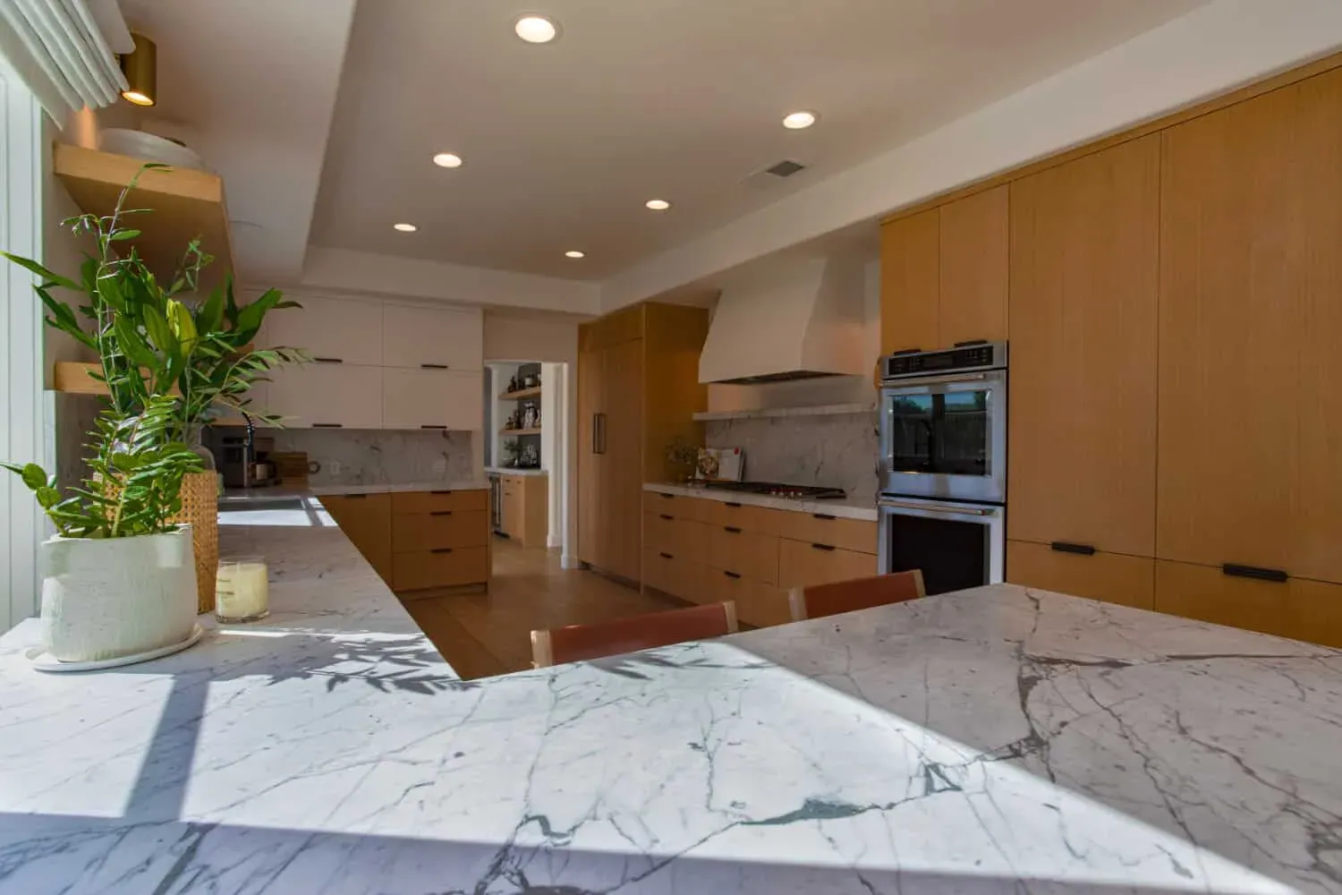 Remodeled Anaheim kitchen with oak cabinetry, open shelving, a white plaster hood and a marble island
