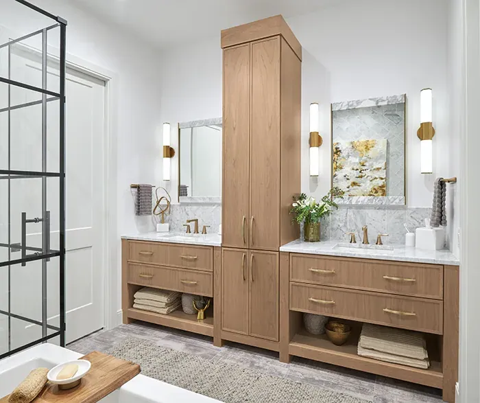 Omega Cabinetry photograph of a double bathroom vanity and linen tower in its Jaxson door style in a warm wood finish, not a Kitchen Cabinets and Beyond project