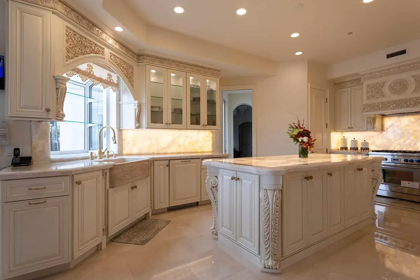 Cream kitchen with a carved island, glass-front upper cabinets and a lit marble backsplash