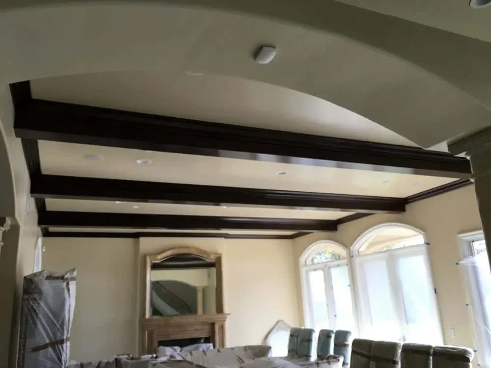 Living room part-way through a remodel, with dark stained ceiling beams, arched windows and furniture wrapped in plastic