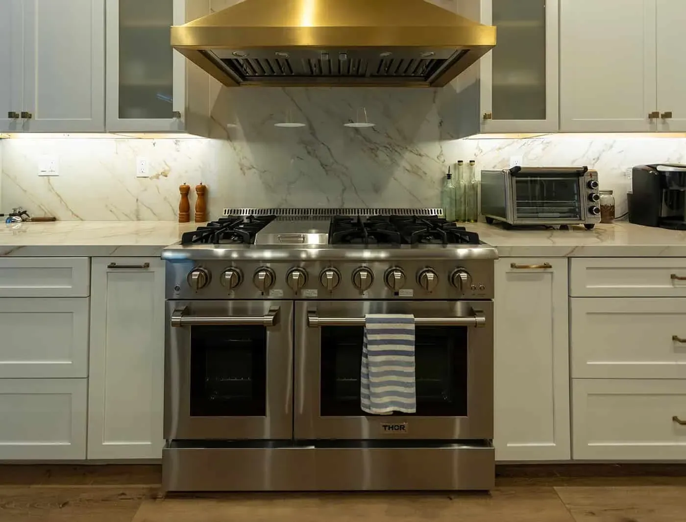 Stainless double-oven range beneath a brass hood and a marble slab backsplash