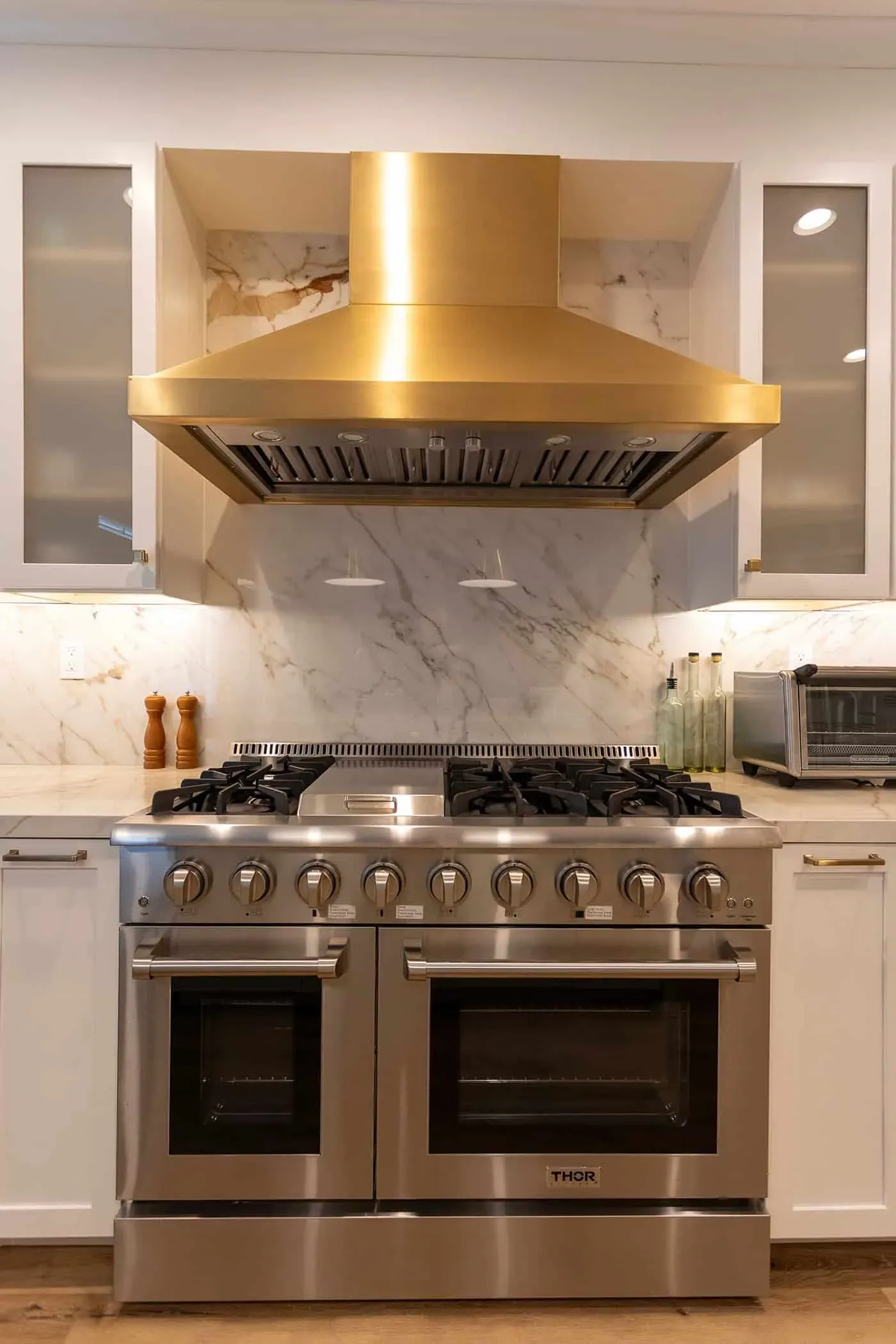 Marble slab backsplash rising behind a stainless professional range beneath a brass hood