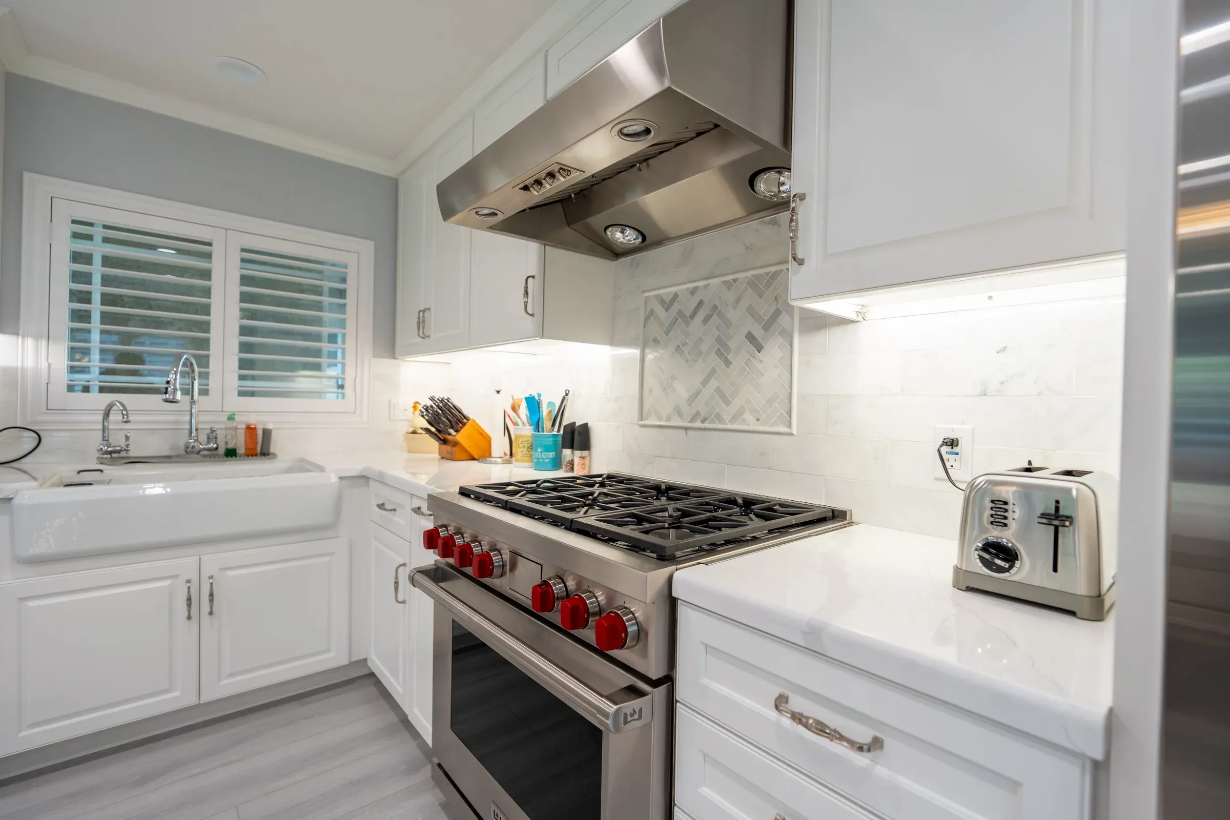 Stainless range under a hood with a marble herringbone inset in the backsplash