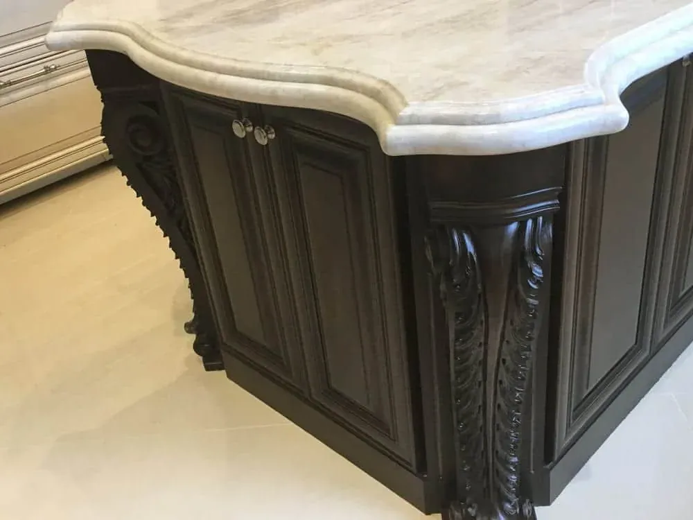 Thick travertine island top with an ogee edge on dark carved cabinetry