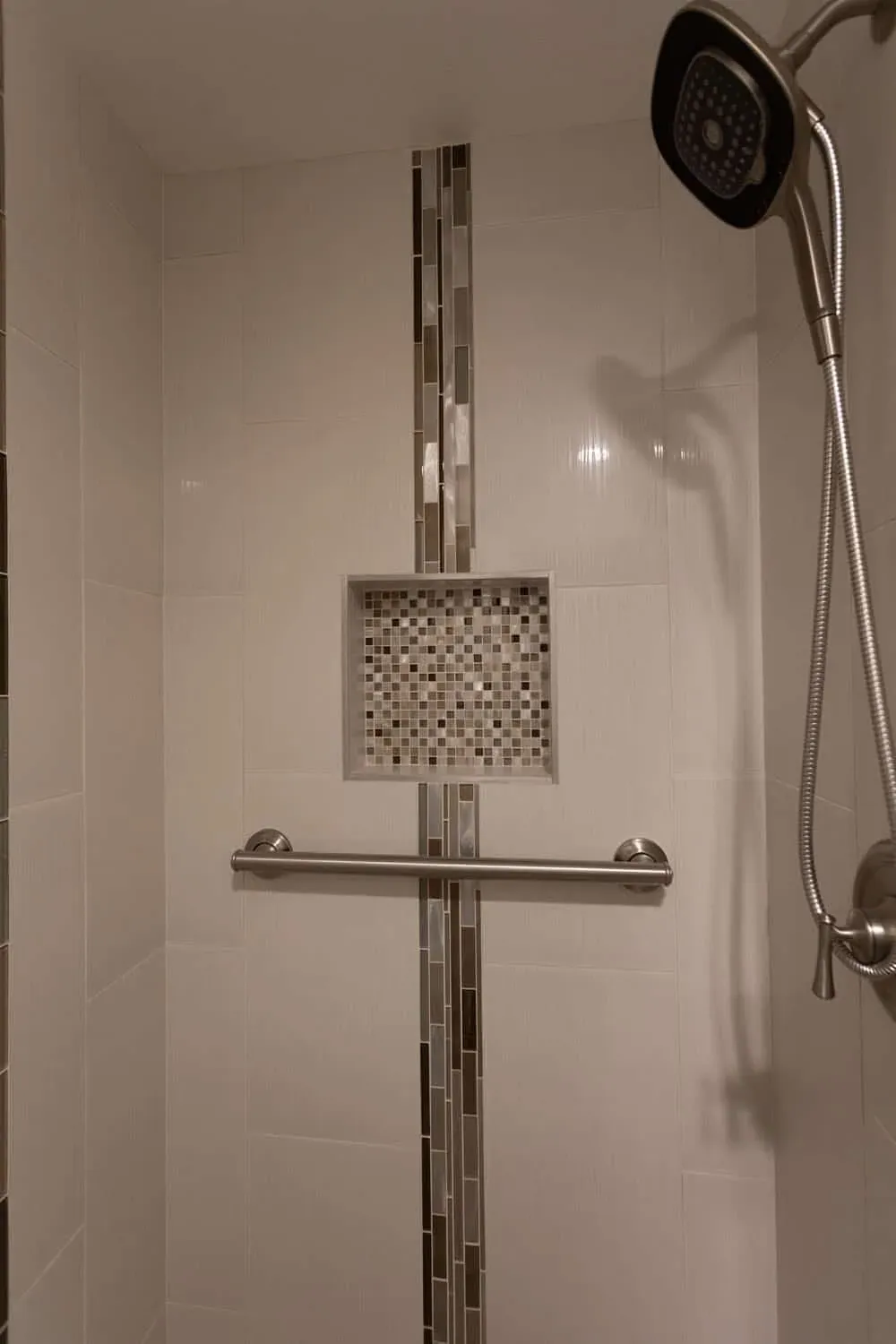 Tiled shower with a mosaic accent strip, a recessed niche, a grab rail and a handheld shower