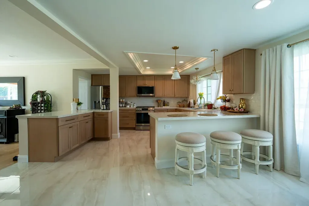 Kitchen with light oak shaker cabinets, a white peninsula with three upholstered stools and a polished porcelain floor