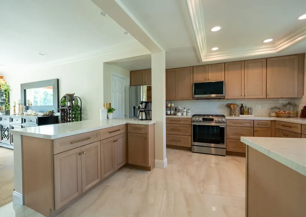 Light oak shaker kitchen seen from the living room past a white column and a cream stone peninsula top