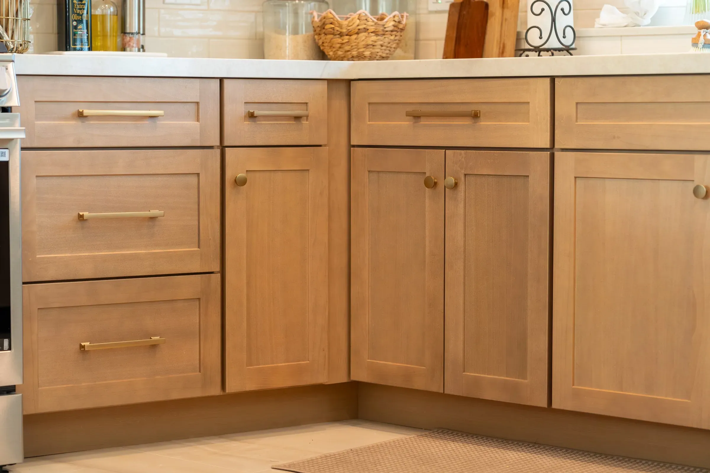 Light oak shaker base cabinets with brass bar pulls and round brass knobs below a cream stone countertop