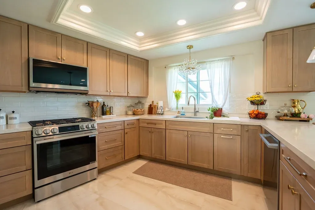 U-shaped kitchen of light oak shaker cabinets around a window with a crystal chandelier and a stainless gas range