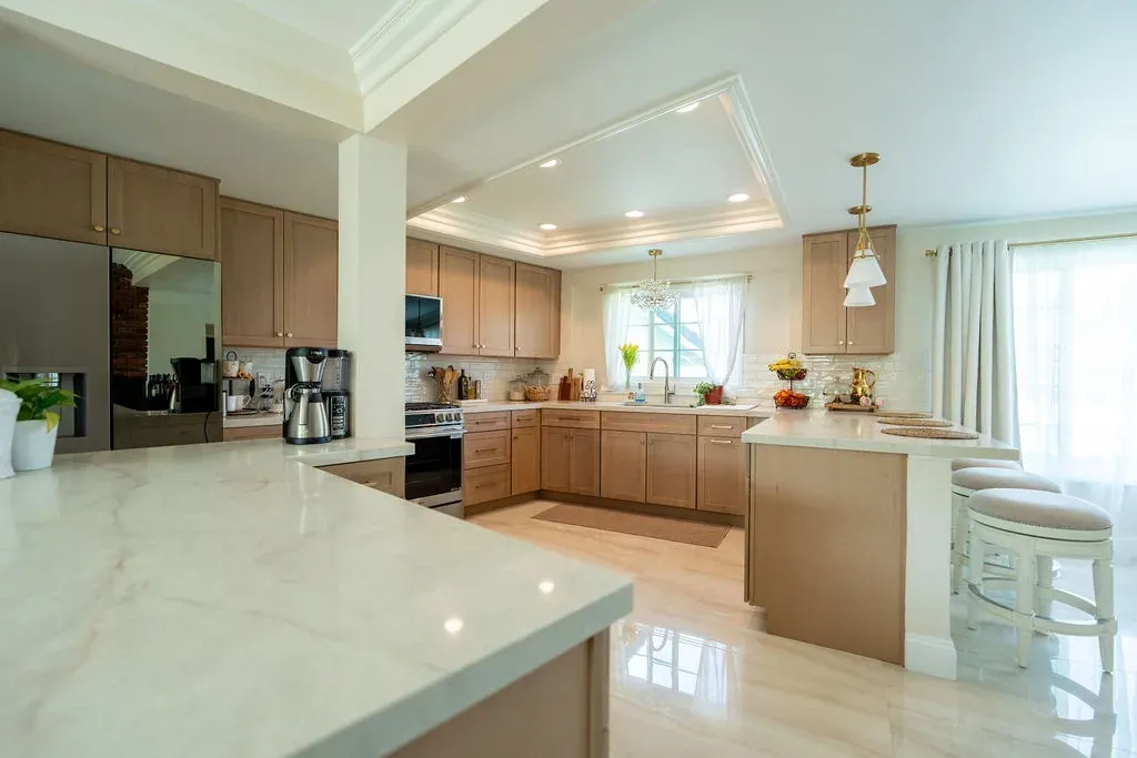 Veined cream stone countertop in the foreground with the light oak kitchen and peninsula stools beyond