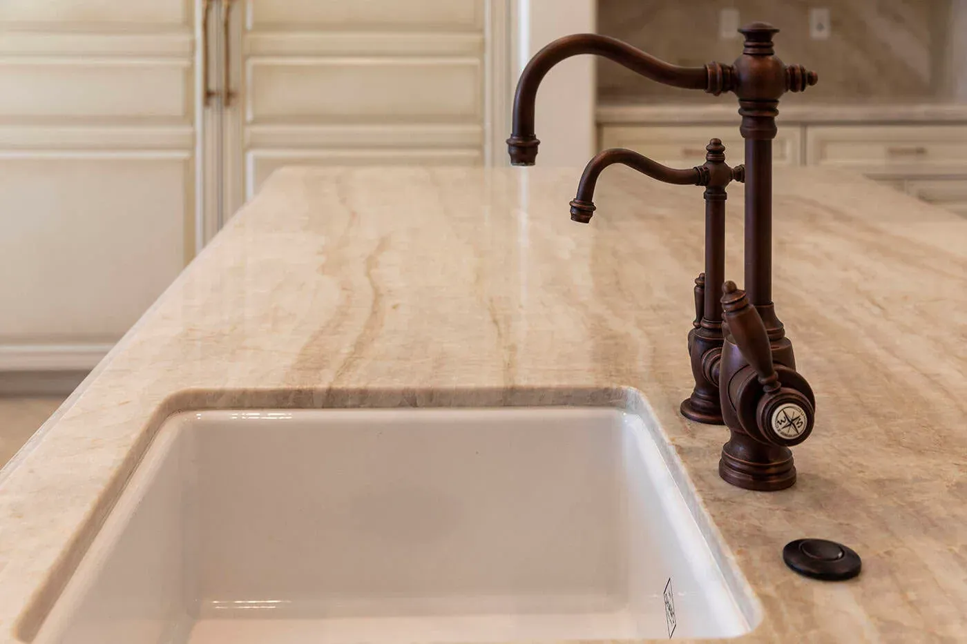 Undermount white sink cut into a veined stone worktop with an oil-rubbed bronze tap