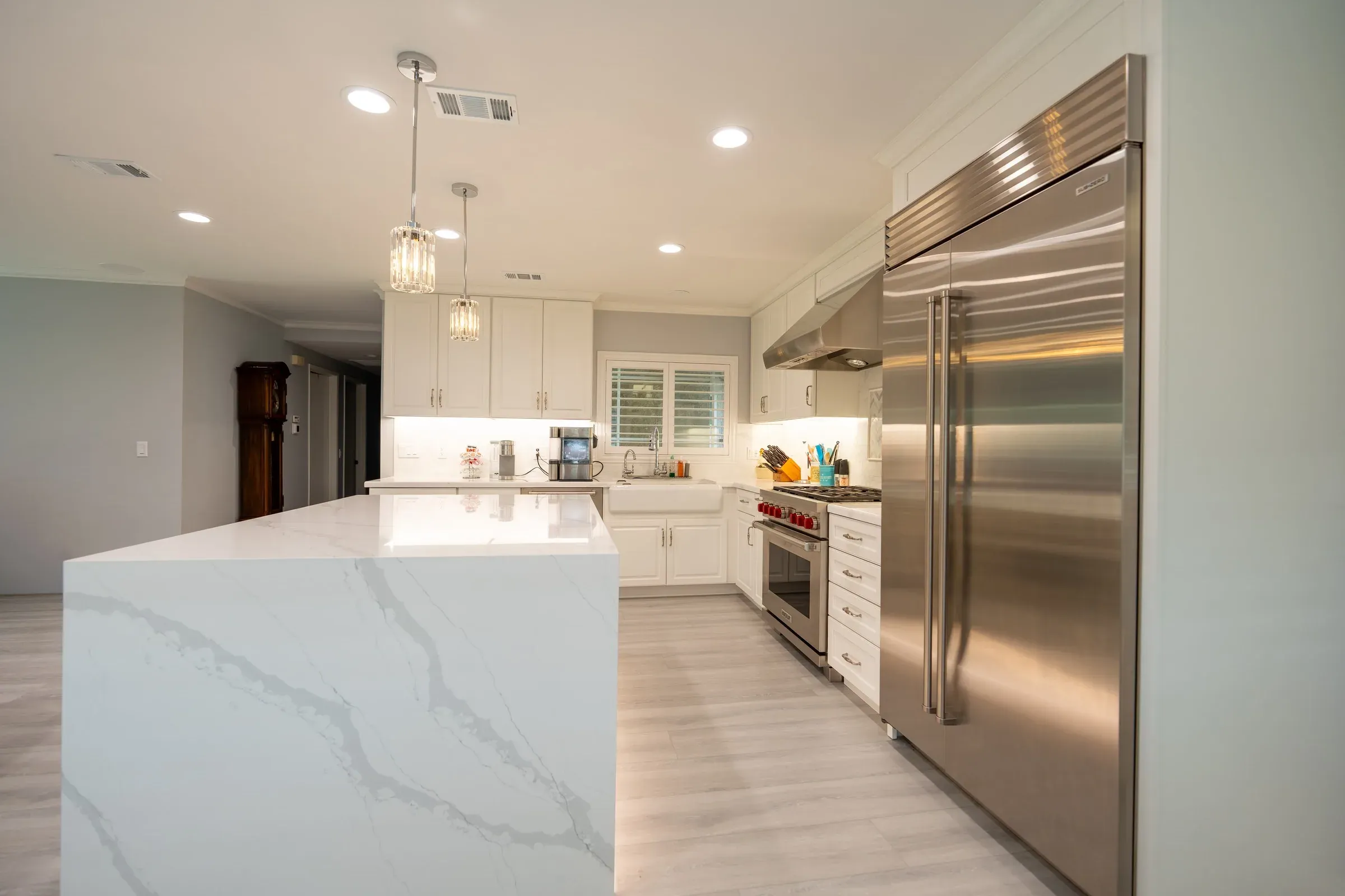 Quartz waterfall island beside a built-in stainless refrigerator in a white kitchen
