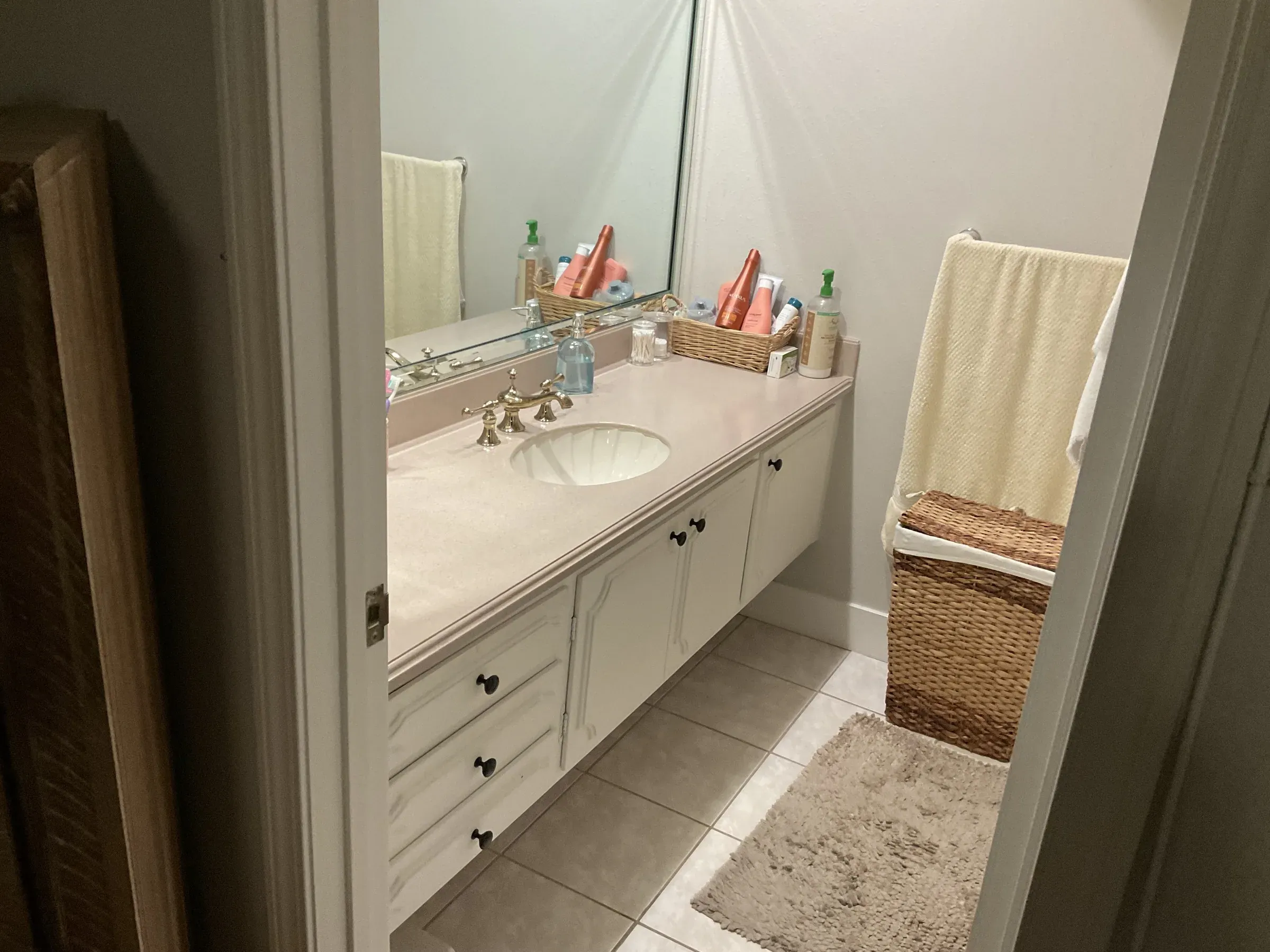 Westminster bathroom before the remodel, with a long white vanity, a pale one-piece top and a wall mirror
