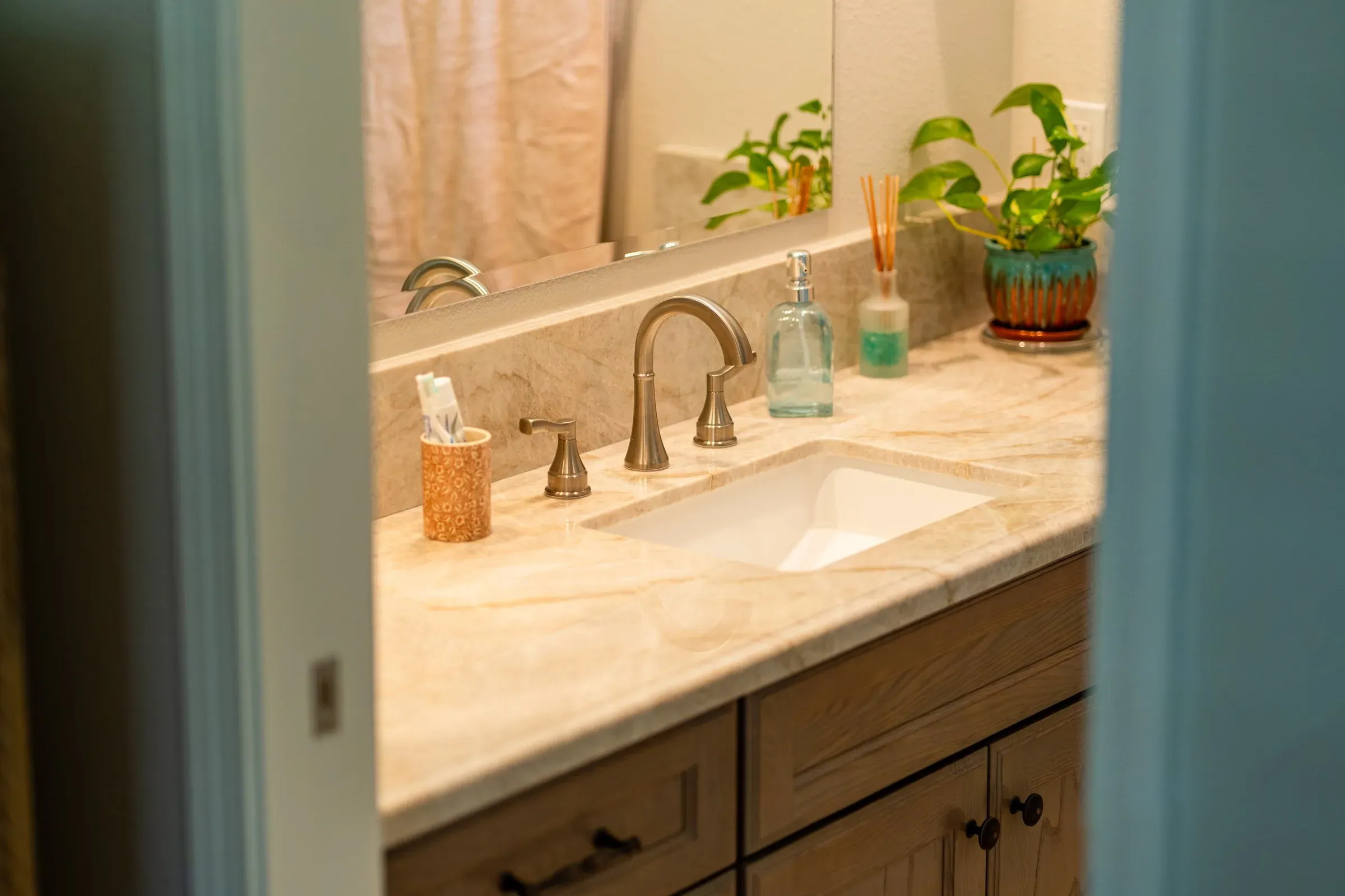 Wood vanity with a stone top and a brushed nickel faucet seen through a bathroom doorway