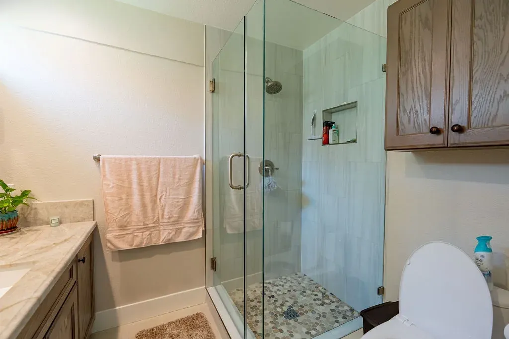 Frameless glass shower with a river pebble floor, pale vertical wall tile and a recessed niche