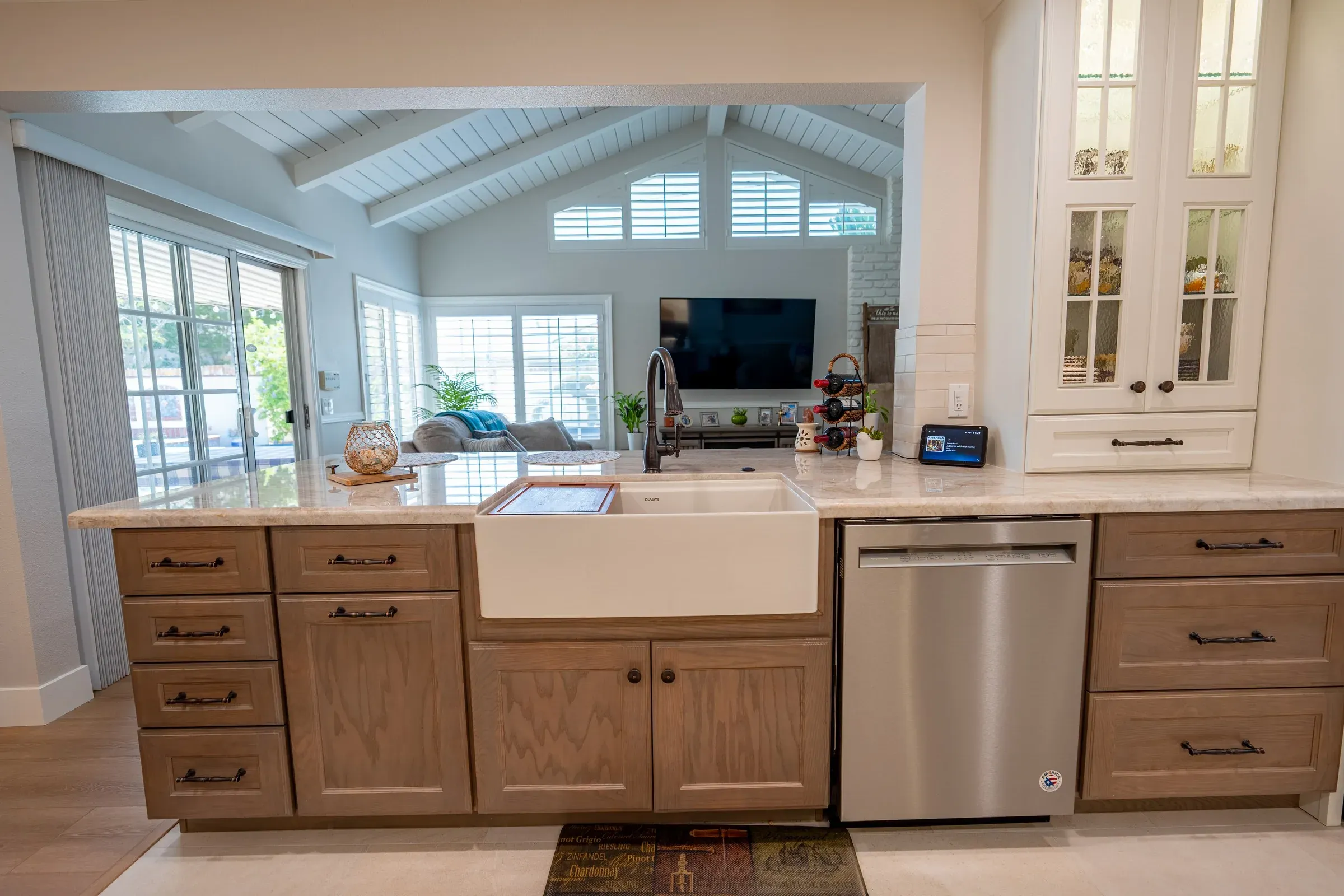 Oak cabinets with bronze pulls around a white farmhouse sink under the pass-through to the family room